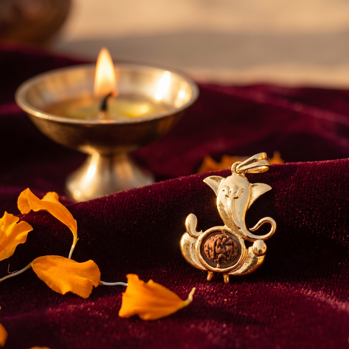 Siddhi Ganesha Rudraksha pendant on maroon velvet beside a brass diya